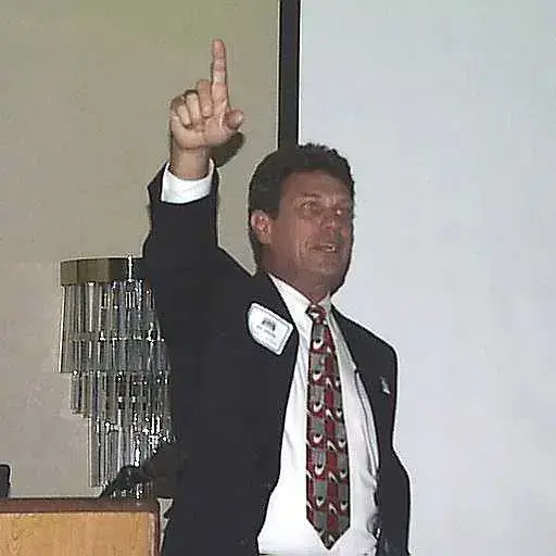 Dressed in a suit with a name tag, Bill Dexter speaks passionately from a podium.